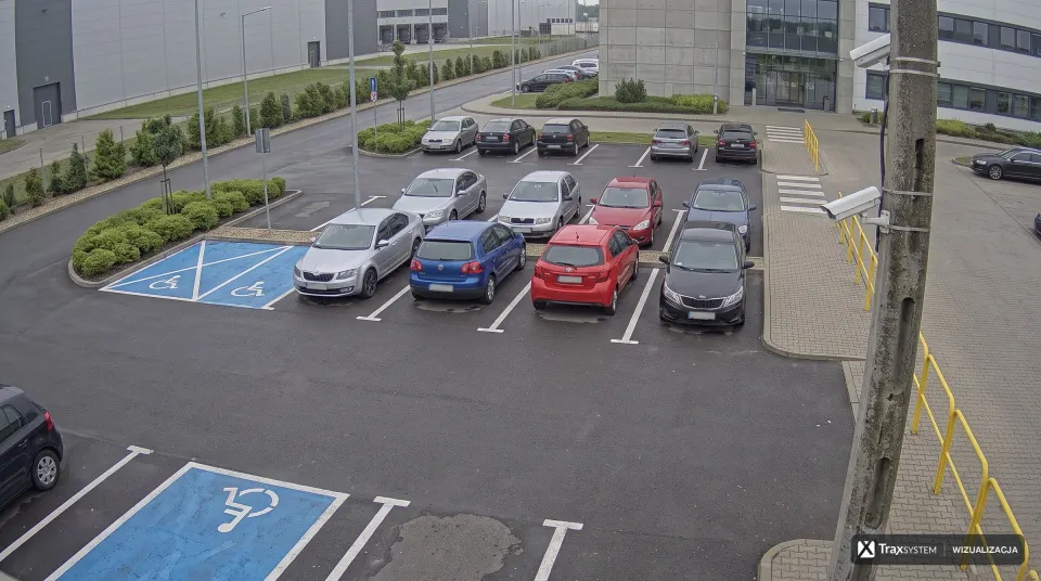 Parking samochodów osobowych przed budynkiem biurowo-magazynowym, widok z kamery na słupie.