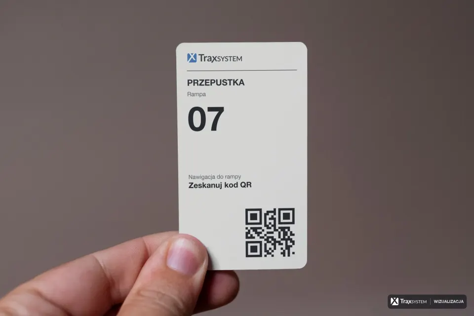 Dłoń trzyma w pionie białą kartę na jednolitym szarobrązowym tle. Na kartę naniesiono przepustkę z kiosku: logo TraxSystem, napis Przepustka, numer rampy 07 i kod QR z dopiskiem o nawigacji do rampy; kciuk zasłania lewy dolny róg karty.